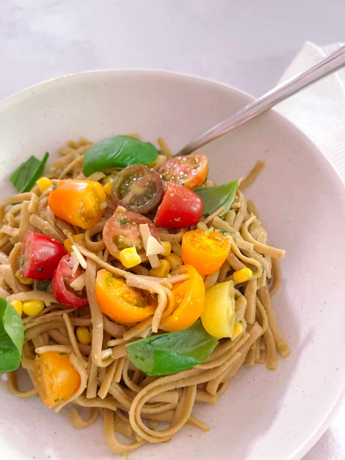 close up of a bowl of creamy avocado basil pasta with tomatoes and corn with a spoon