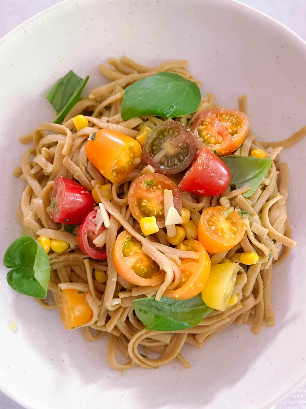 close up of creamy avocado basil pasta with tomatoes and corn, garnished with fresh basil leaves