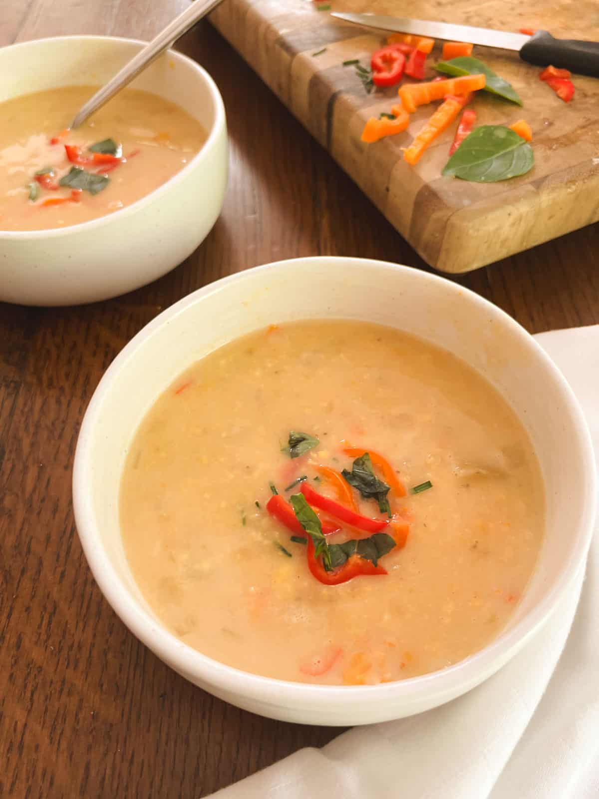 close up of two bowls of garnished lightened-up Instant Pot corn chowder with cutting board in the background