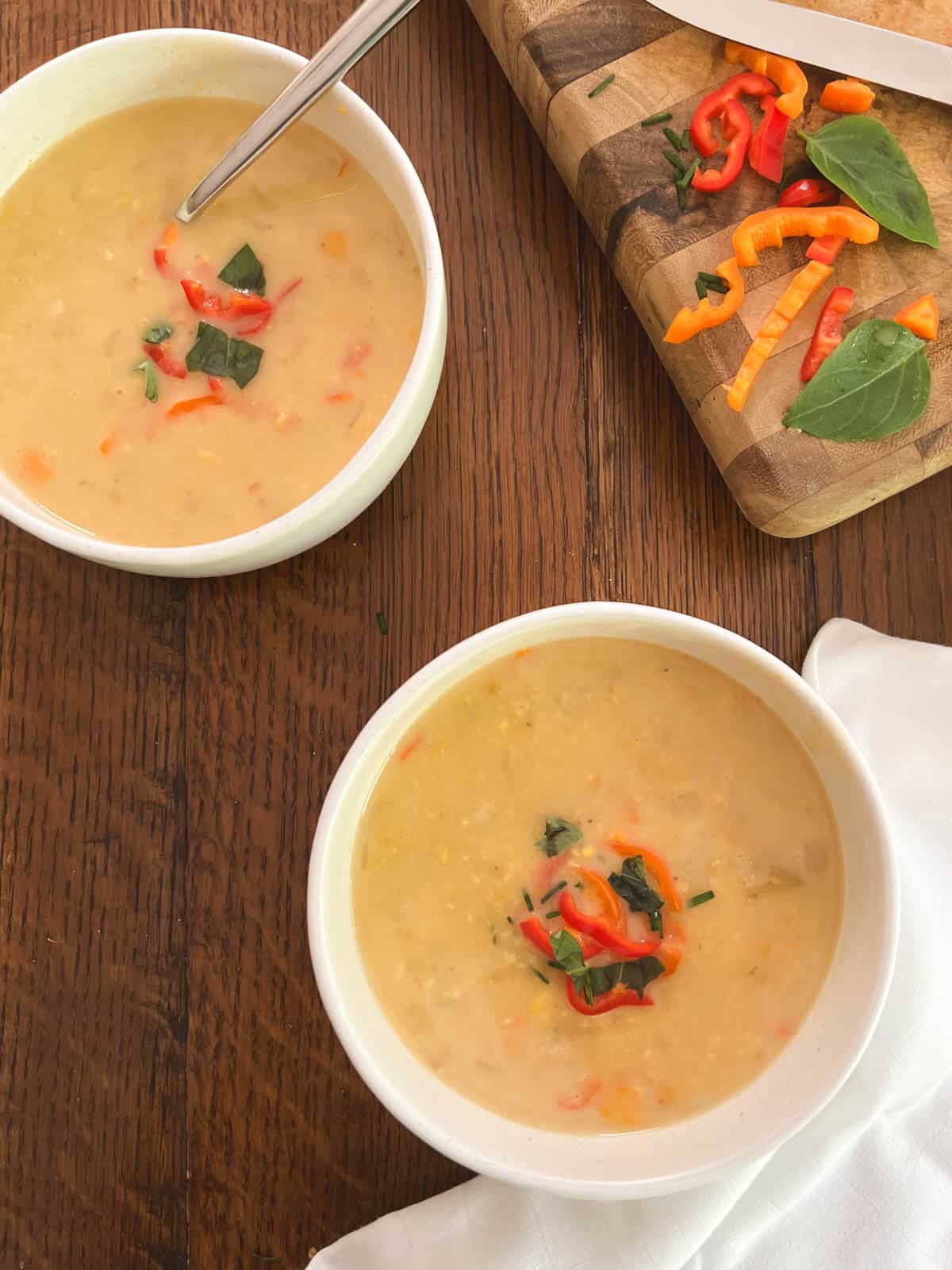 two bowls of lightened-up Instant Pot corn chowder and a cutting board with chopped peppers and basil