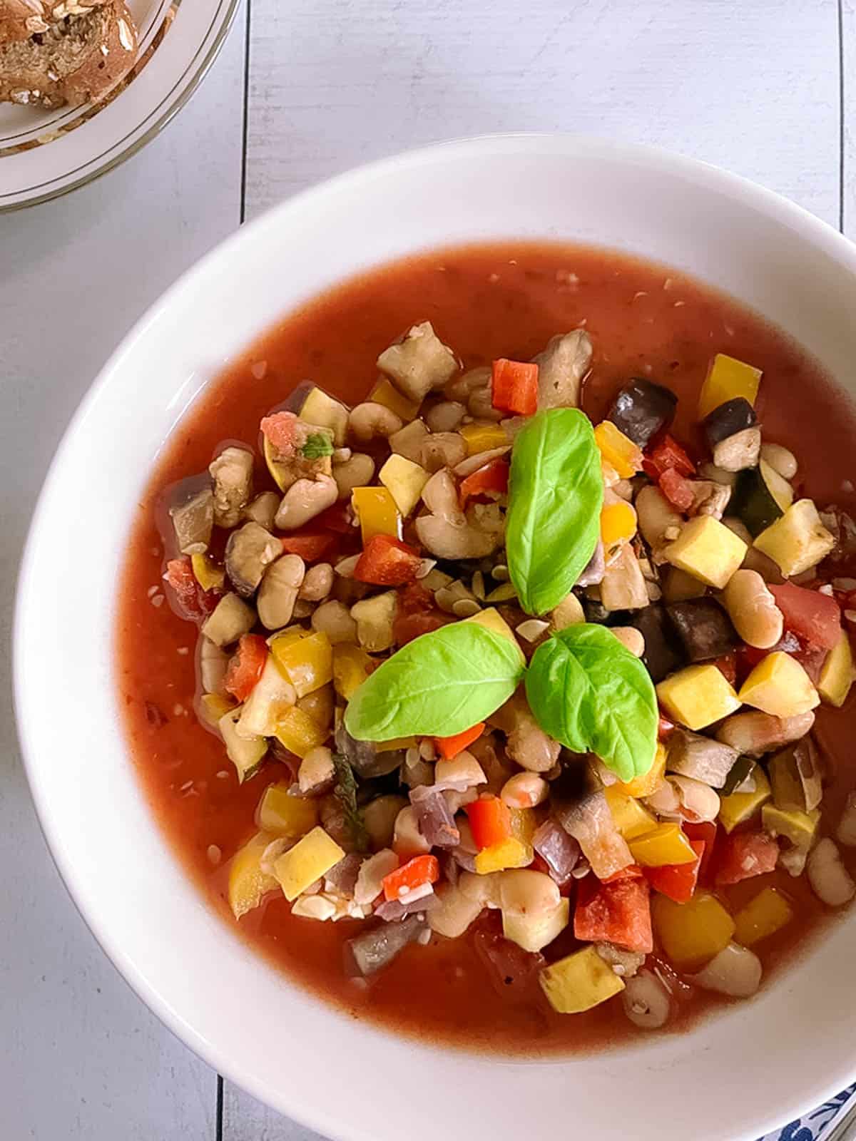 closeup overhead view of a bowl of slow cooker ratatouille with white beans and a plate of sliced wheat bread