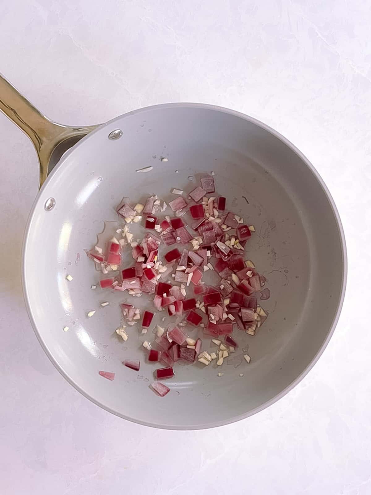 skillet containing cooked diced red onion and minced garlic