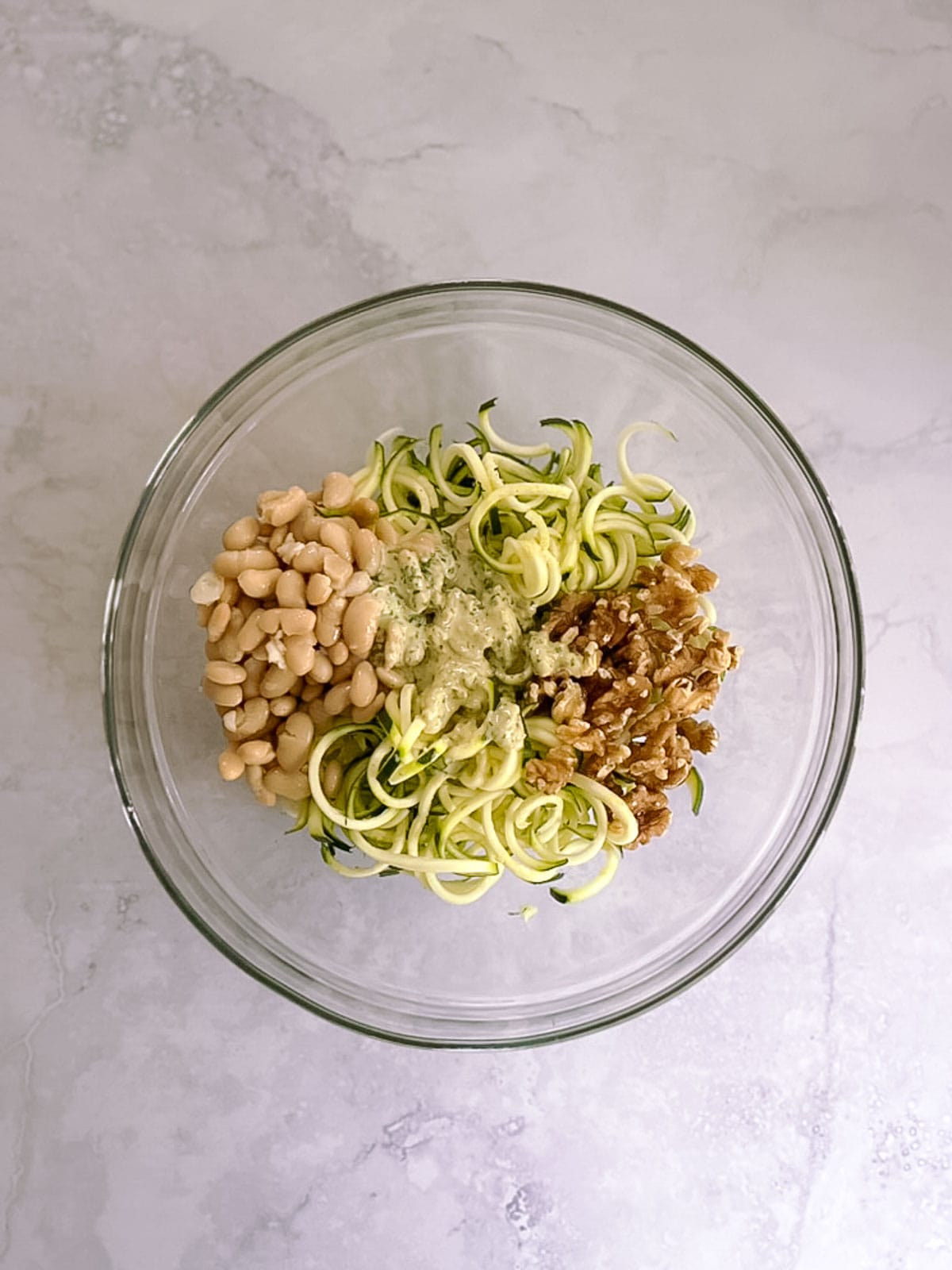 overhead of bowl containing unmixed ingredients for zucchini noodles with tahini basil sauce