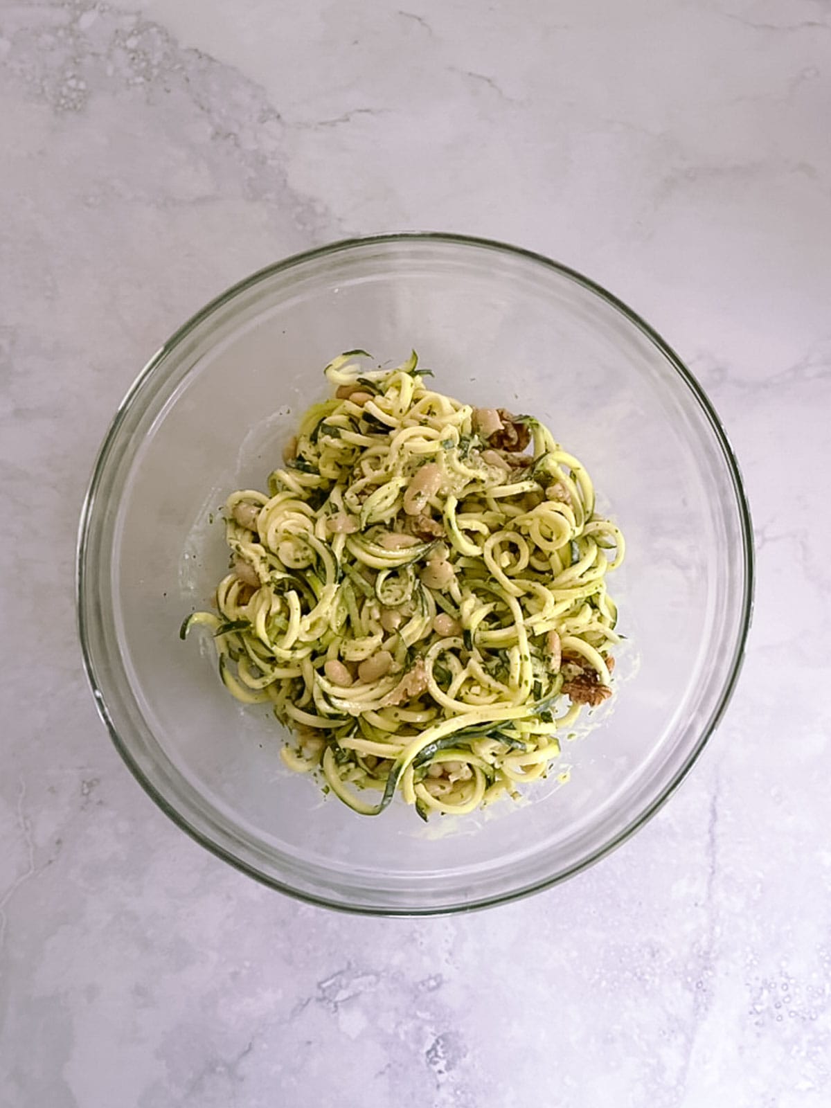 overhead of bowl containing mixed ingredients for zucchini noodles with tahini basil sauce