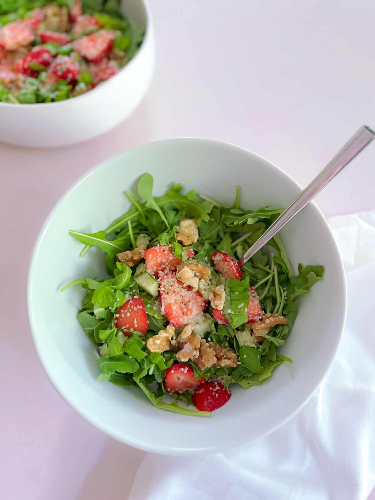 bowl of strawberry basil salad with champagne vinaigrette with fork; large serving bowl of salad in the background