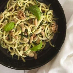 close up of bowl of zucchini noodles with tahini basil sauce with napkin on the side