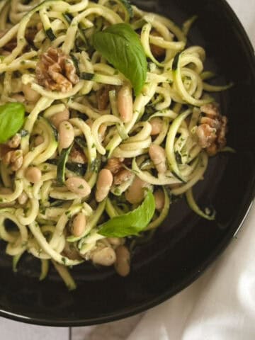 close up of bowl of zucchini noodles with tahini basil sauce with napkin on the side