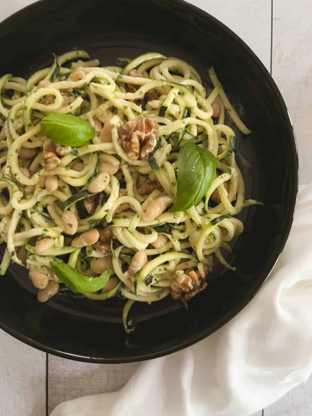 closeup overhead view of a bowl of zucchini noodles with tahini basil sauce