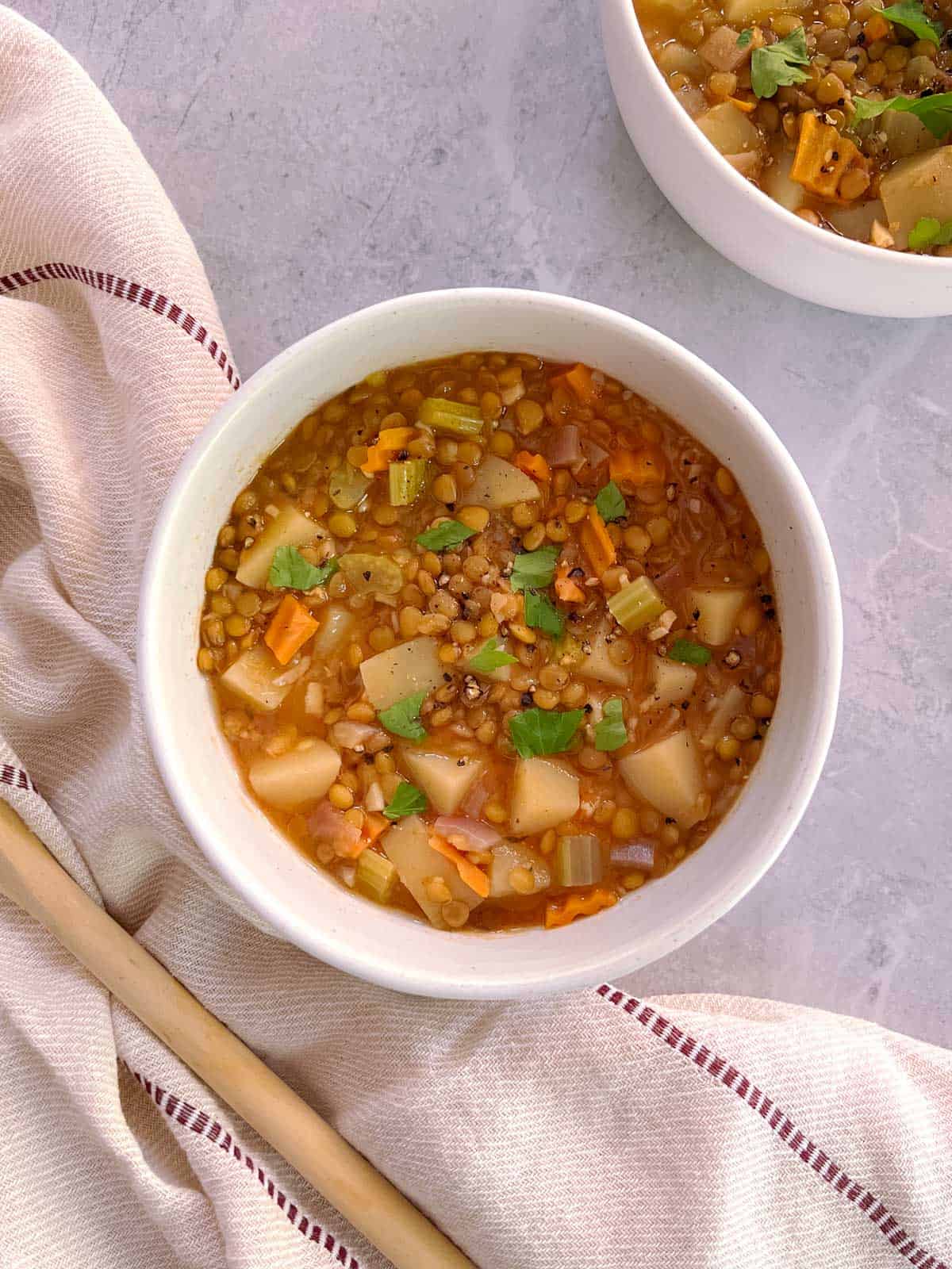 overhead of bowl of essential instant pot lentil soup with bowl in the background, cloth napkin, and wooden spoon