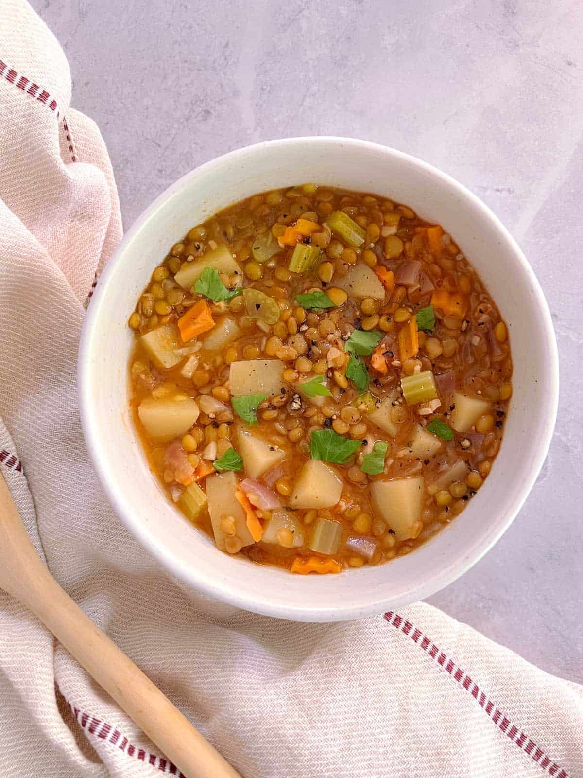 overhead of bowl of essential instant pot lentil soup with cloth napkin and wooden spoon