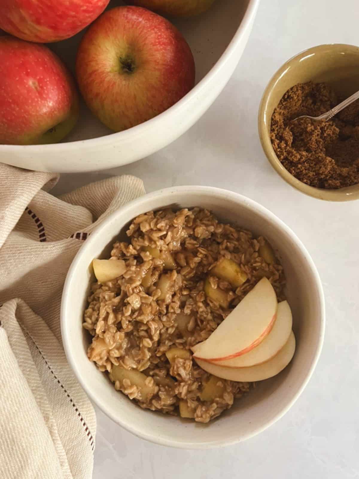 bowl of one-pot apple cinnamon oatmeal with small bowl of coconut sugar and large bowl of apples