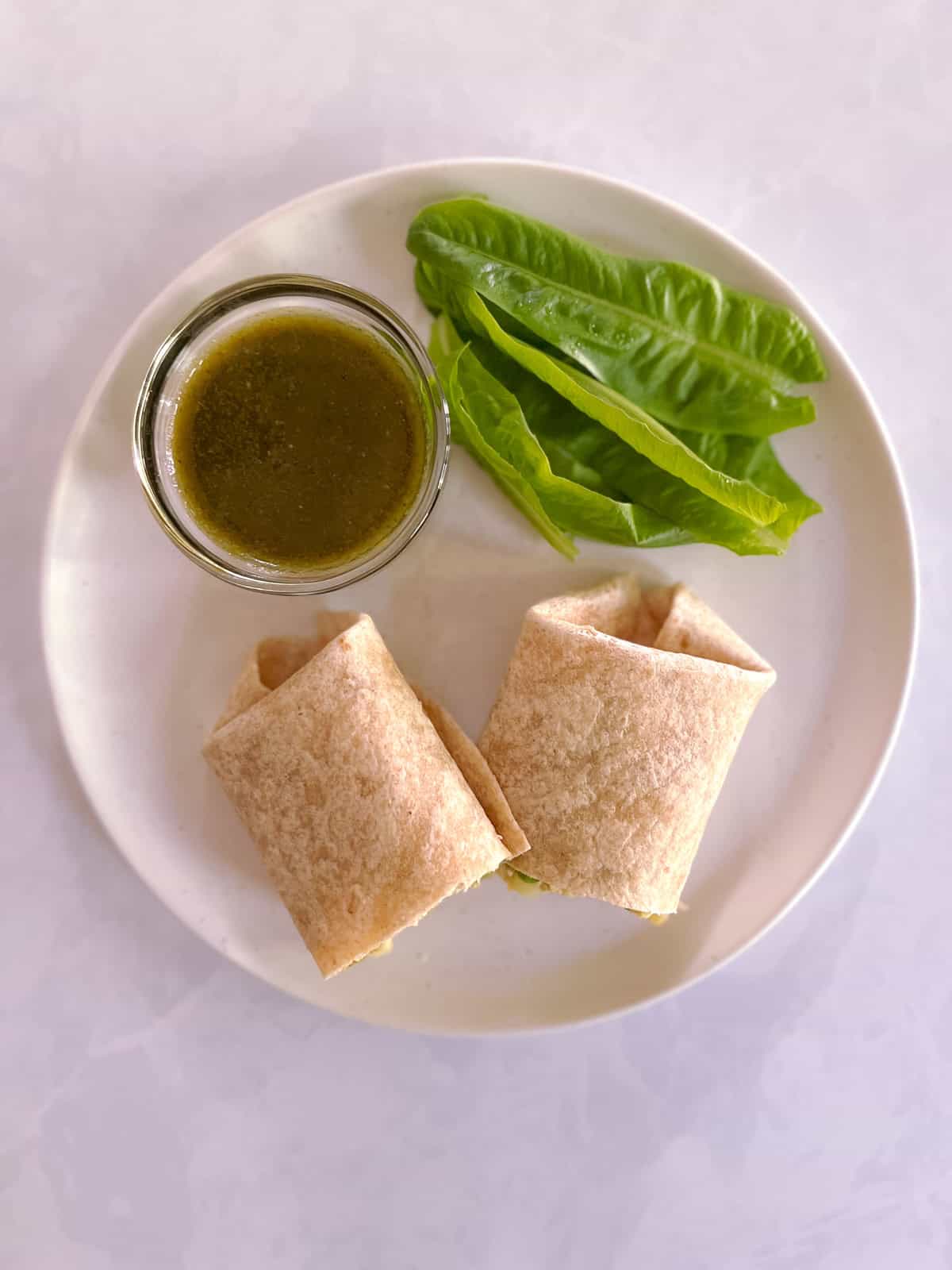 overhead view of plate with sliced potato and pea samosa wrap, chutney, and side of lettuce