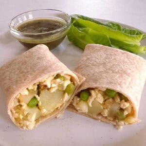 potato and pea samosa wrap sliced in half on a plate with side salad and bowl of mint chutney