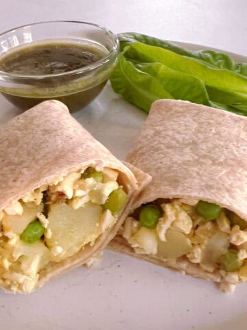 potato and pea samosa wrap sliced in half on a plate with side salad and bowl of mint chutney