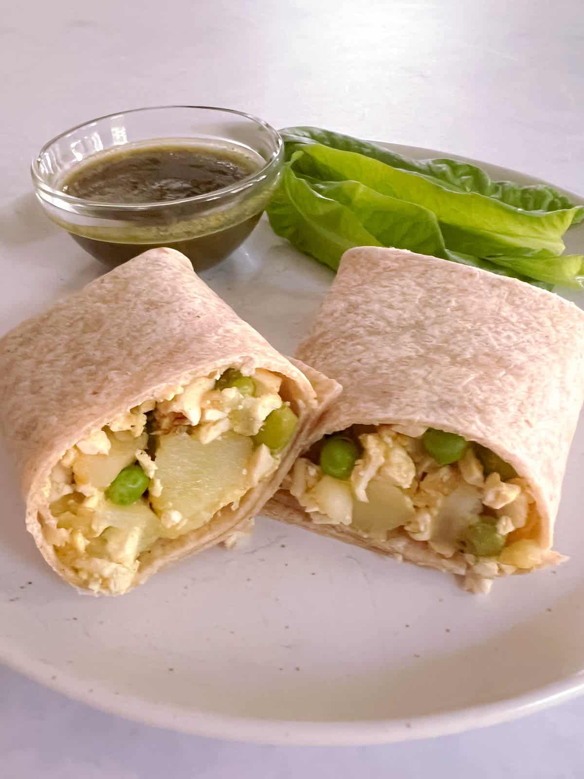 sliced potato and pea samosa wraps on a plate with mint chutney and lettuce