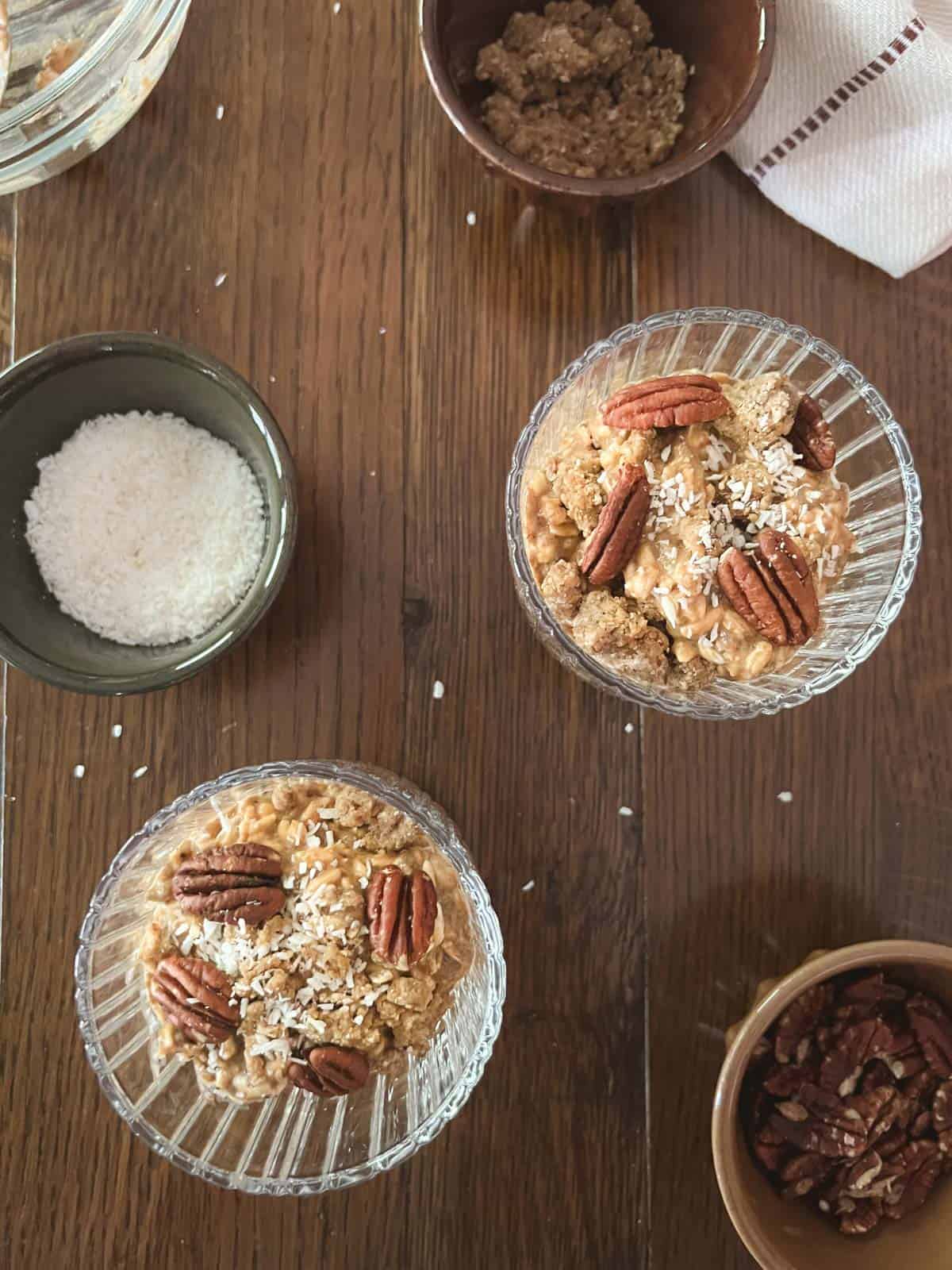 overhead of two parfait dishes of pumpkin spice overnight oats (without yogurt) with small bowls of shredded coconut, pecans, and cookie crumble