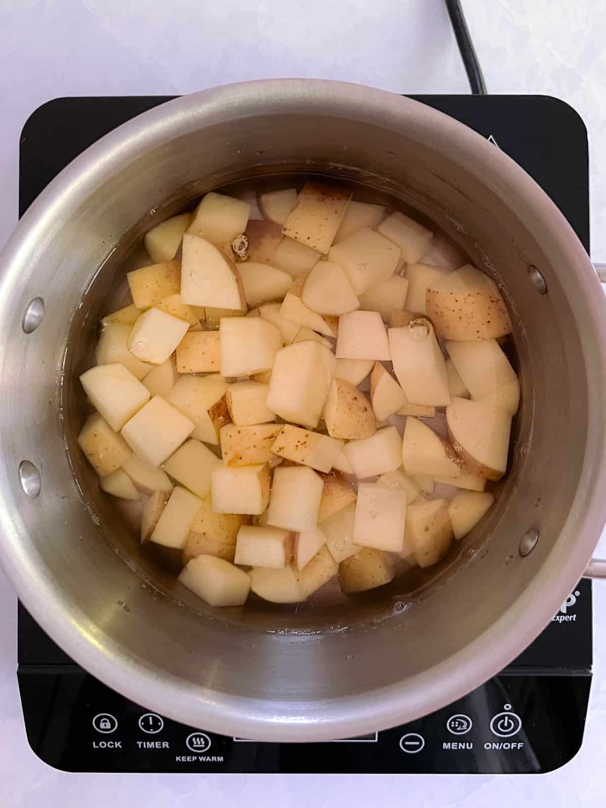 pot of diced potatoes covered with water on a portable cooktop