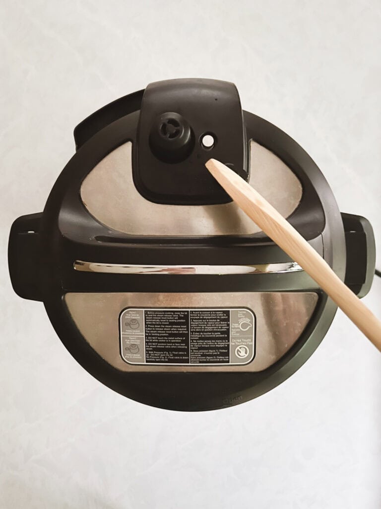 overhead view of sealed instant pot with wooden spoon pressing down the pressure release knob