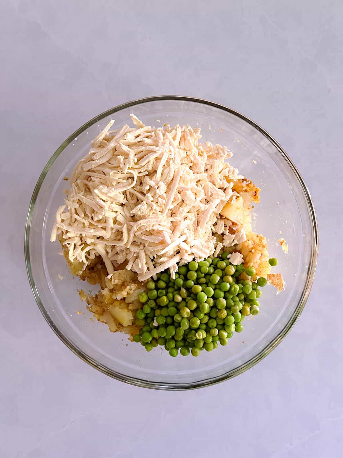 bowl of spiced potatoes with grated tofu and peas added