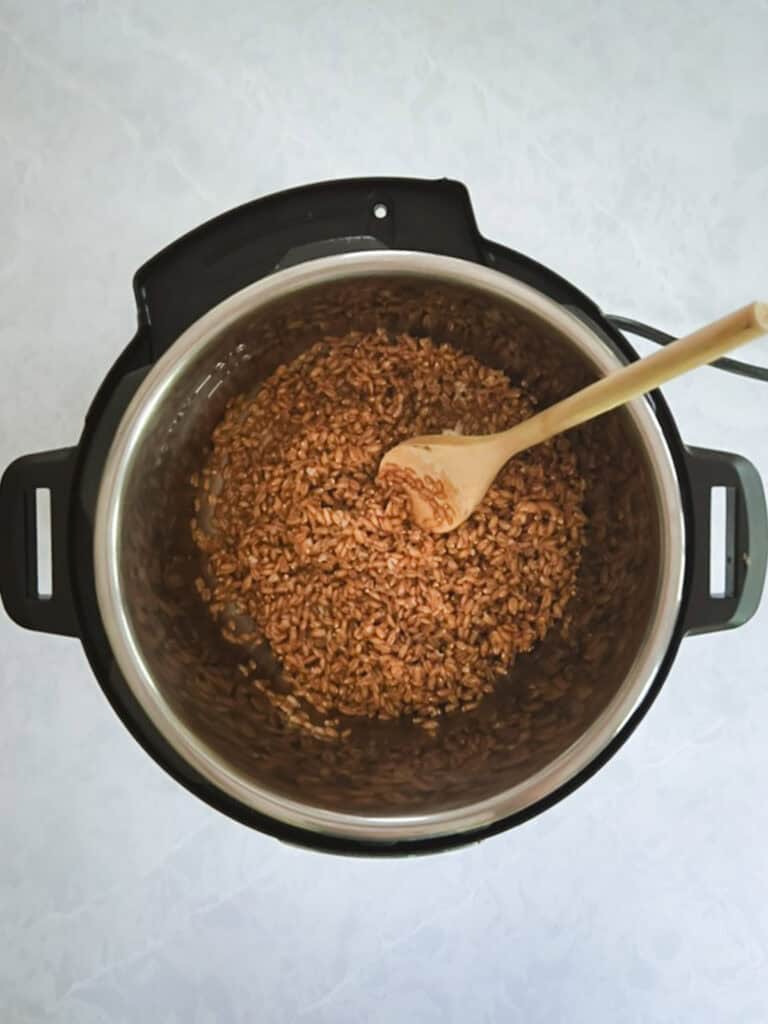 overhead view of instant pot with lid removed and spoon stirring cooked farro inside