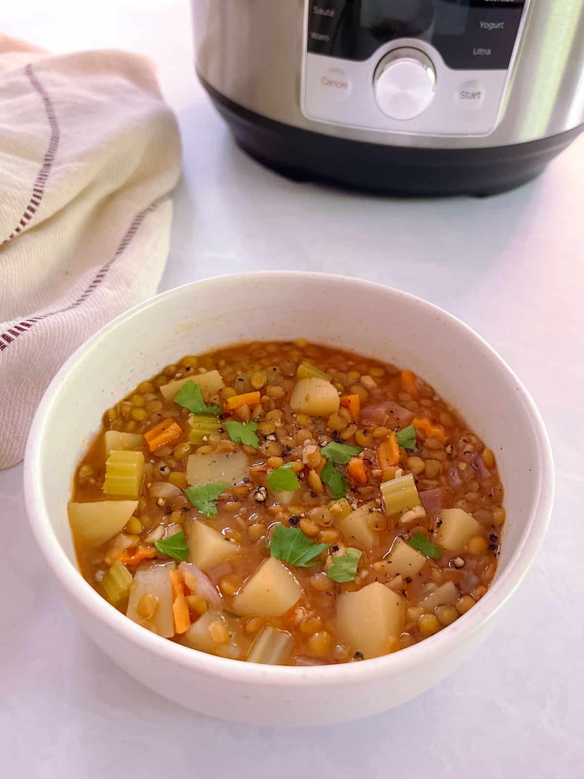 closeup of bowl of essential instant pot lentil soup with cloth napkin and instant pot in the background