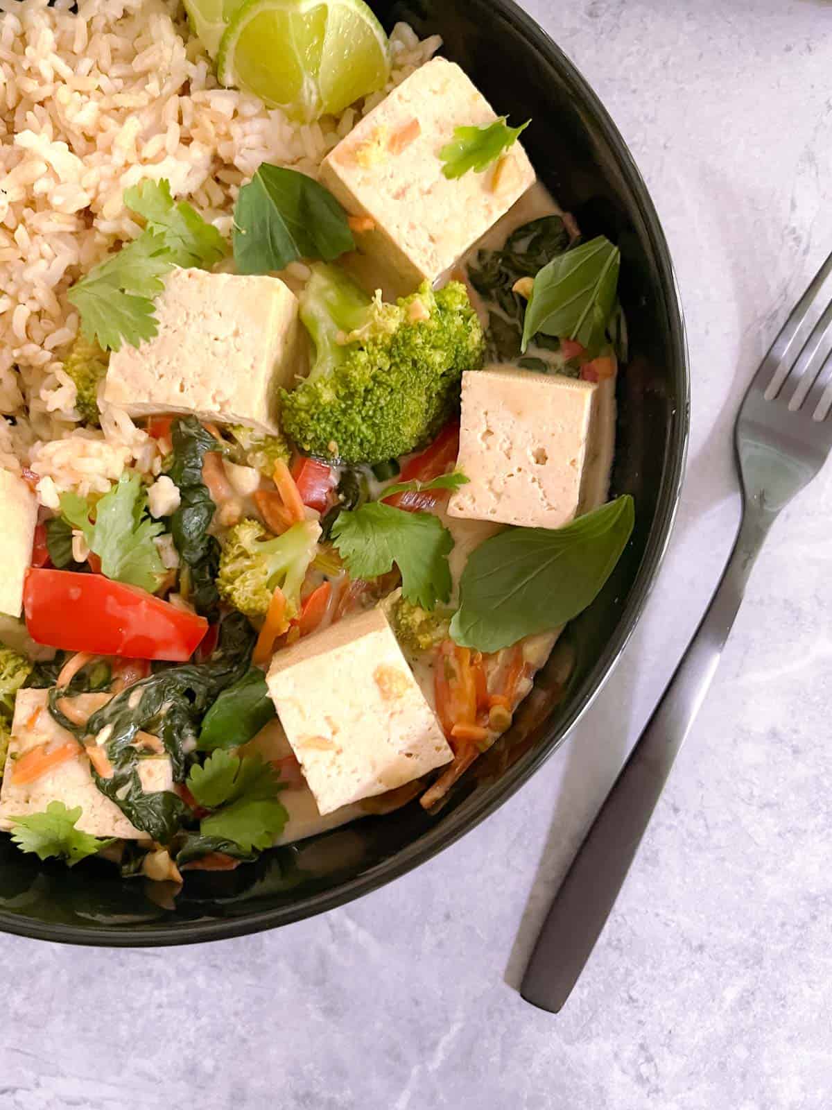 closeup of bowl of easy vegan green curry with tofu and vegetables and a fork