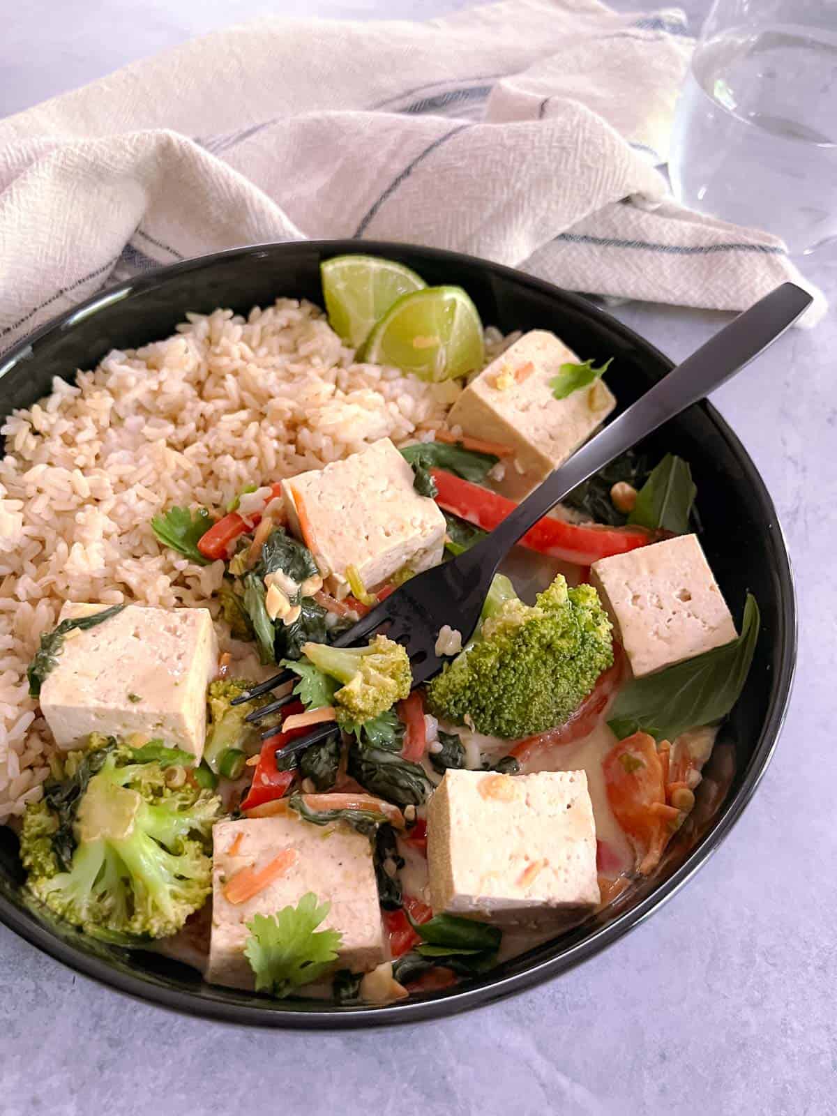 fork in a bowl of easy vegan green curry with tofu and vegetables