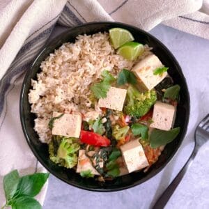 bowl of easy vegan green curry with tofu and vegetables and brown rice with a fork