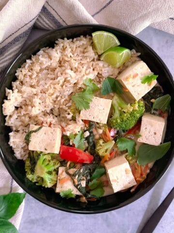 bowl of easy vegan green curry with tofu and vegetables and brown rice with a fork