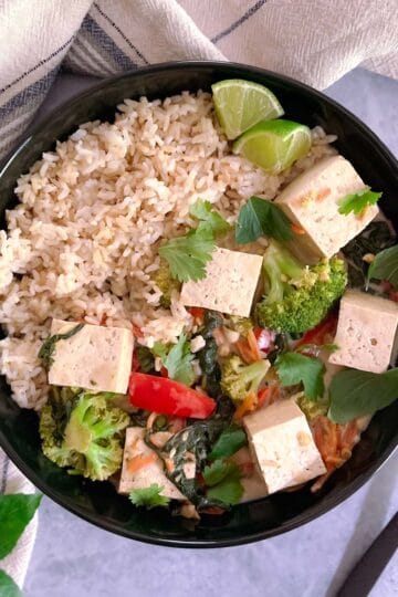 bowl of easy vegan green curry with tofu and vegetables and brown rice with a fork