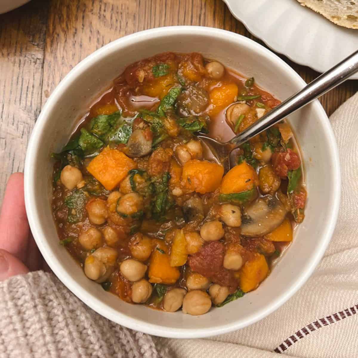 hand cupping a bowl of slow cooker fall harvest ratatouille with a spoon