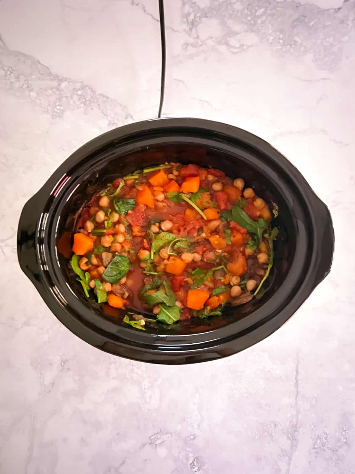 cooked fall harvest ratatouille in a slow cooker with  spinach stirred in