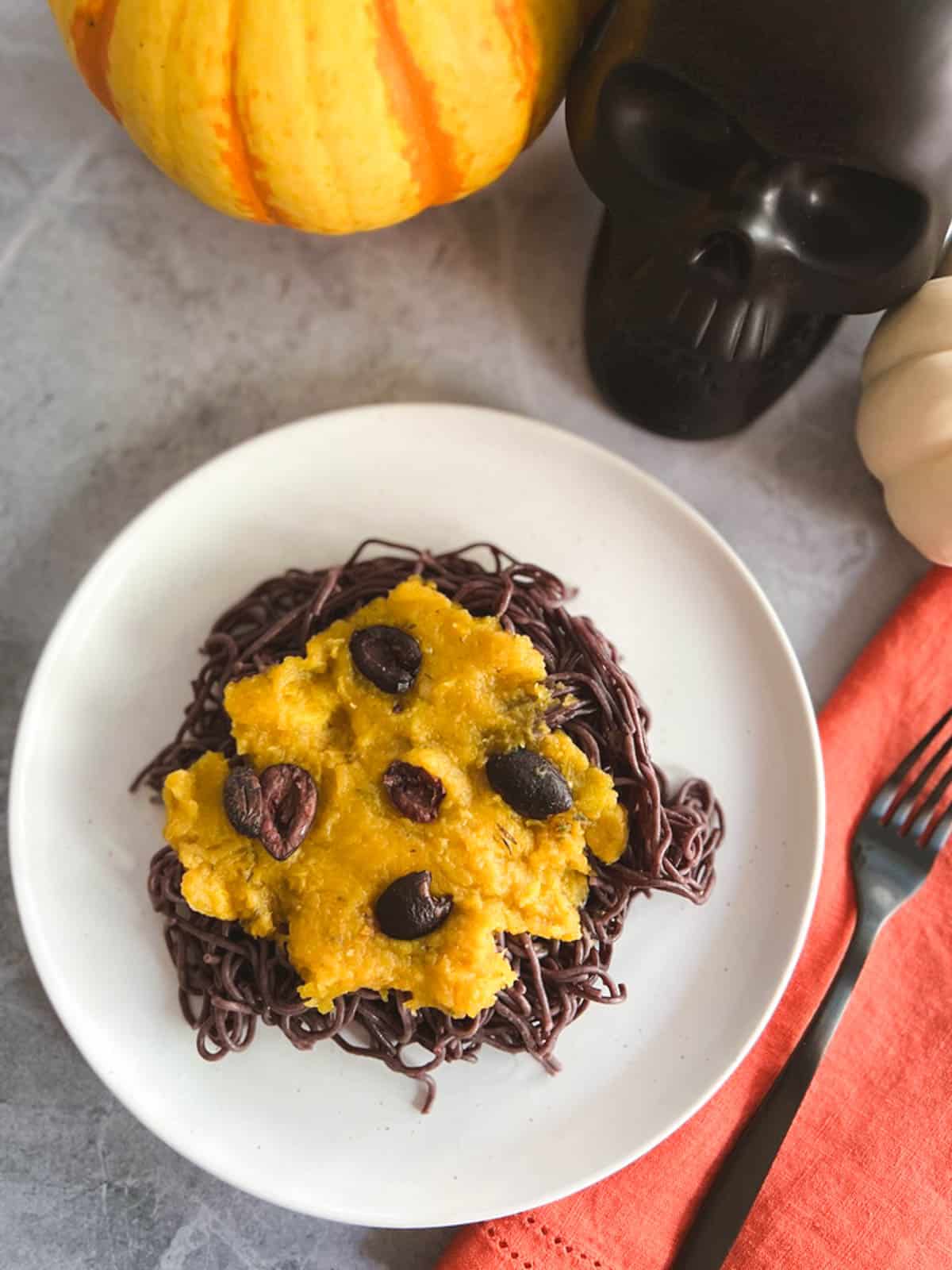 plate of vegan Halloween pasta with a ceramic skull and pumpkins in the background 