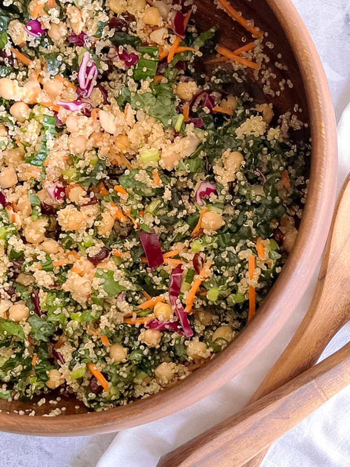 closeup of part of a large wooden bowl of autumn quinoa salad with wooden serving utensils