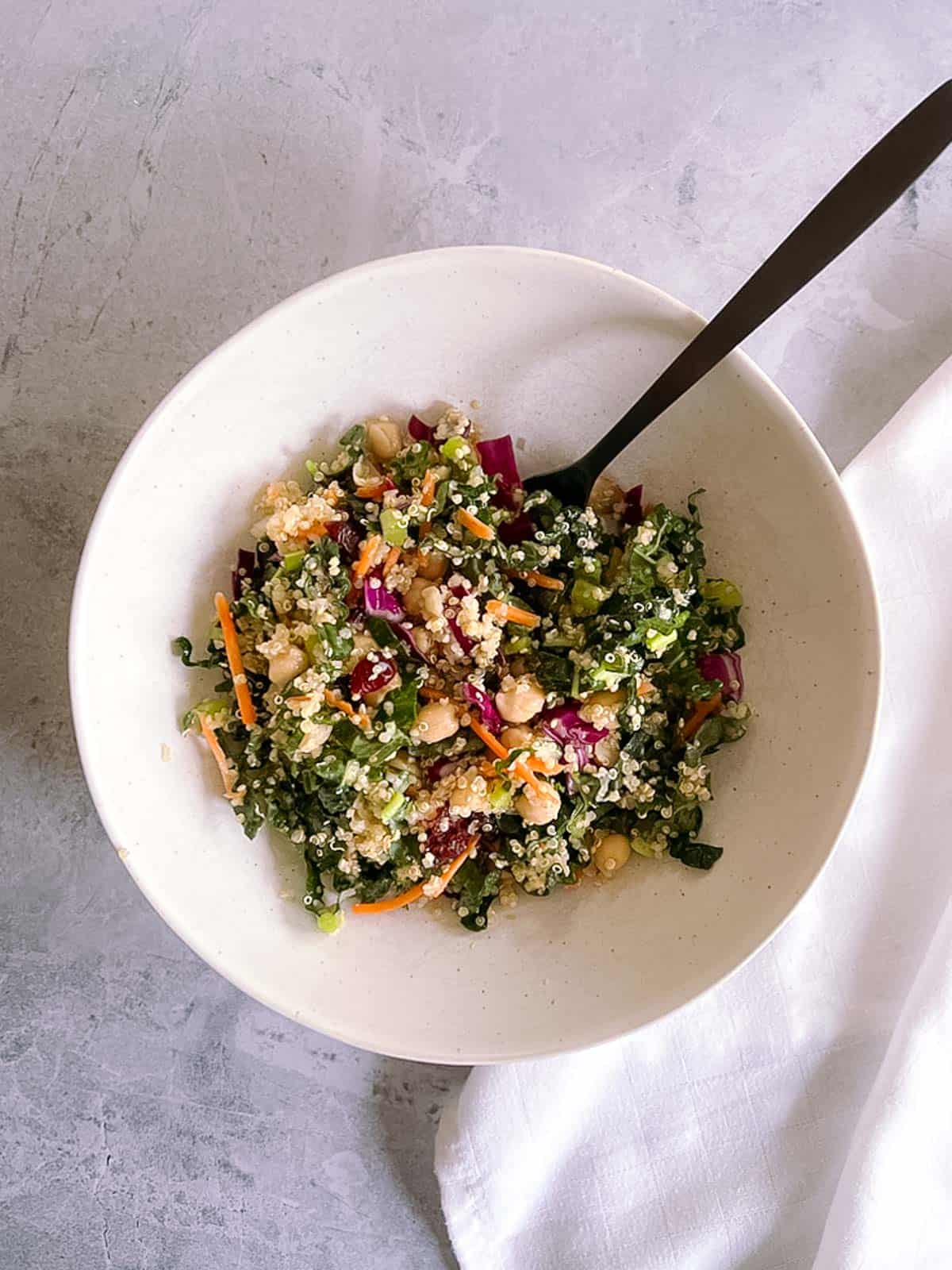 white bowl of autumn quinoa salad with a black fork in it and a white napkin to the right