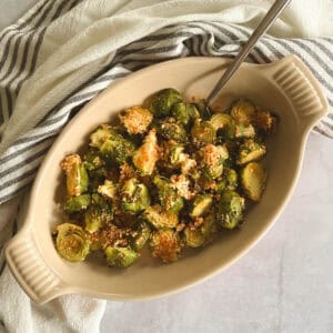 serving dish containing crispy brussels sprouts with spicy maple syrup with serving spoon; towel in background