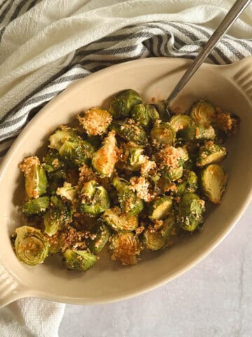 serving dish containing crispy brussels sprouts with spicy maple syrup with serving spoon; towel in background