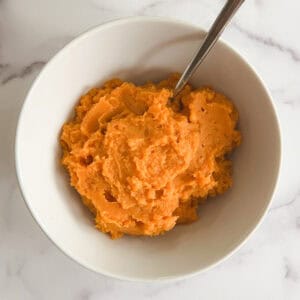 overhead view of instant pot mashed sweet potatoes in a white bowl with a serving spoon in it