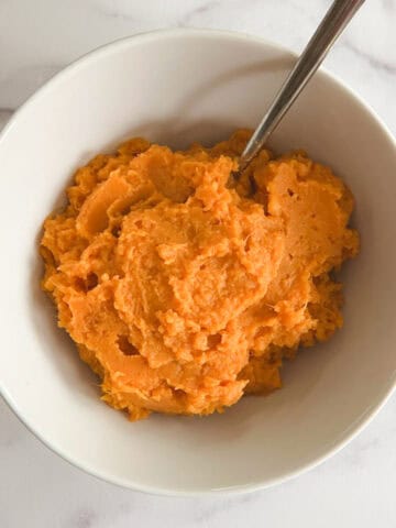 overhead view of instant pot mashed sweet potatoes in a white bowl with a serving spoon in it