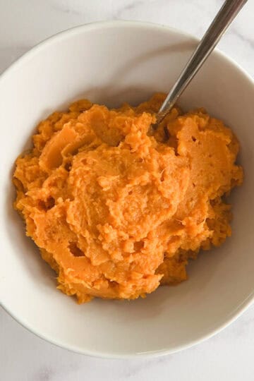 overhead view of instant pot mashed sweet potatoes in a white bowl with a serving spoon in it