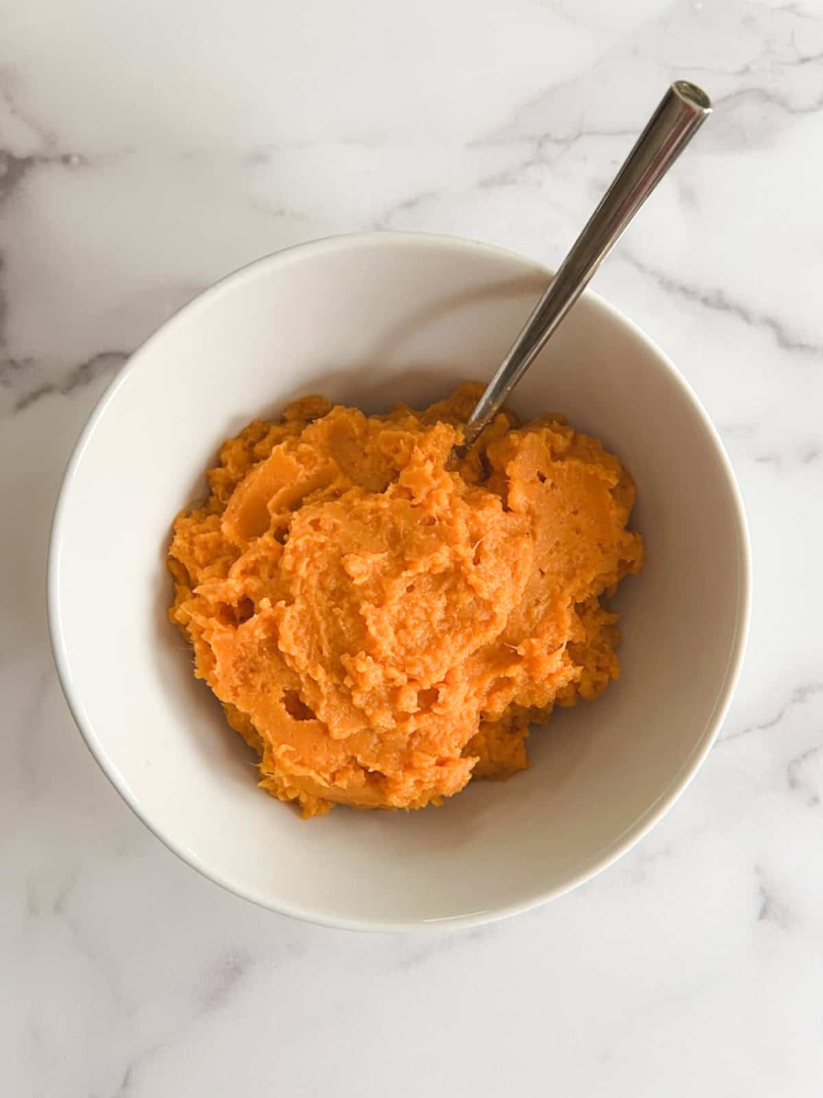 overhead view of a white bowl of instant pot mashed sweet potatoes with a serving spoon in it