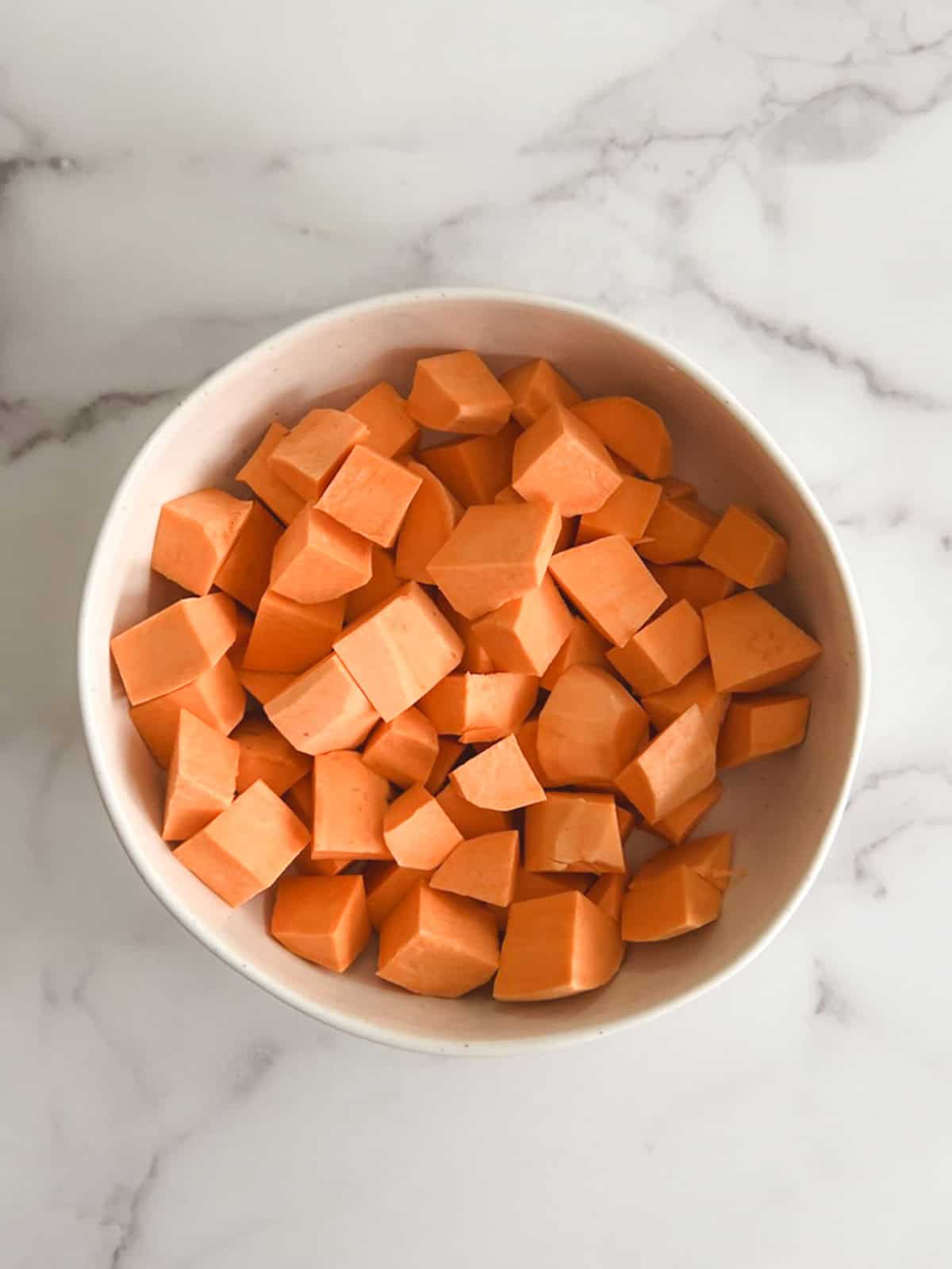 overhead view of a bowl containing peeled and chopped sweet potatoes