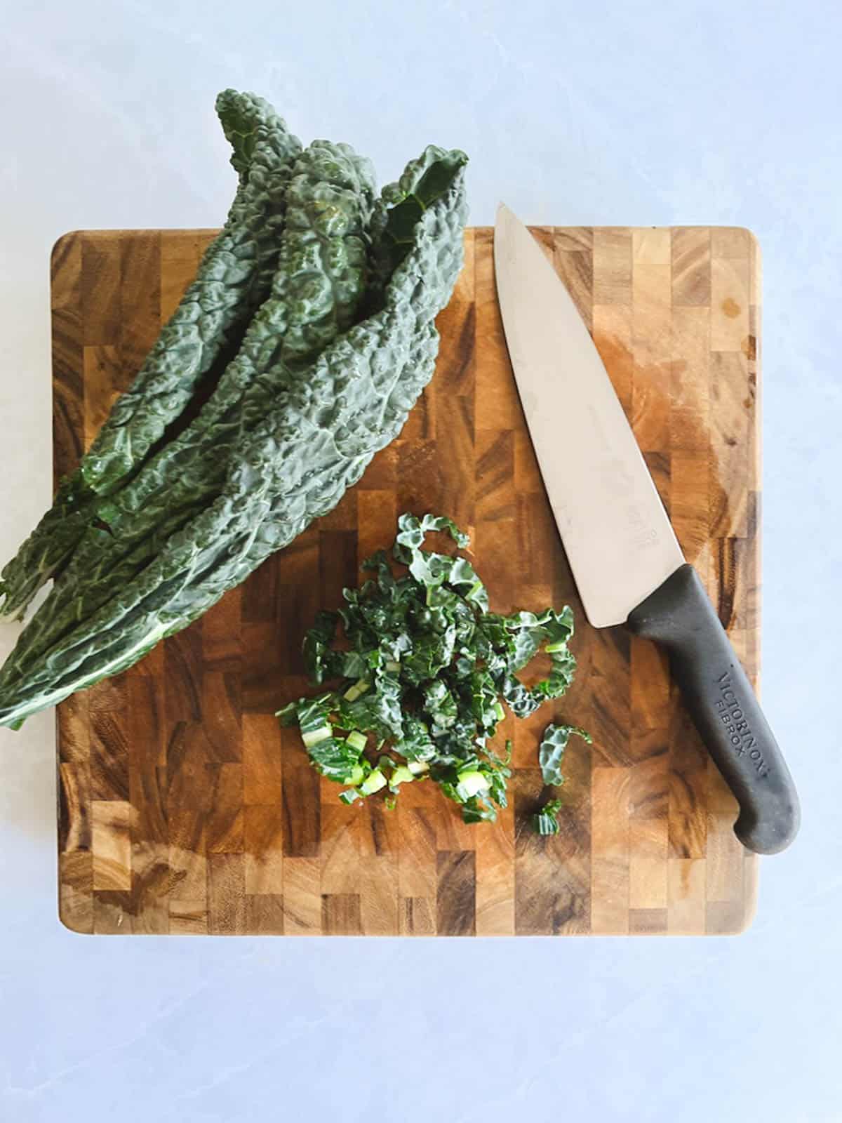 cutting board with whole lacinato kale leaves, some thinly sliced lacinato kale leaves, and chef's knife