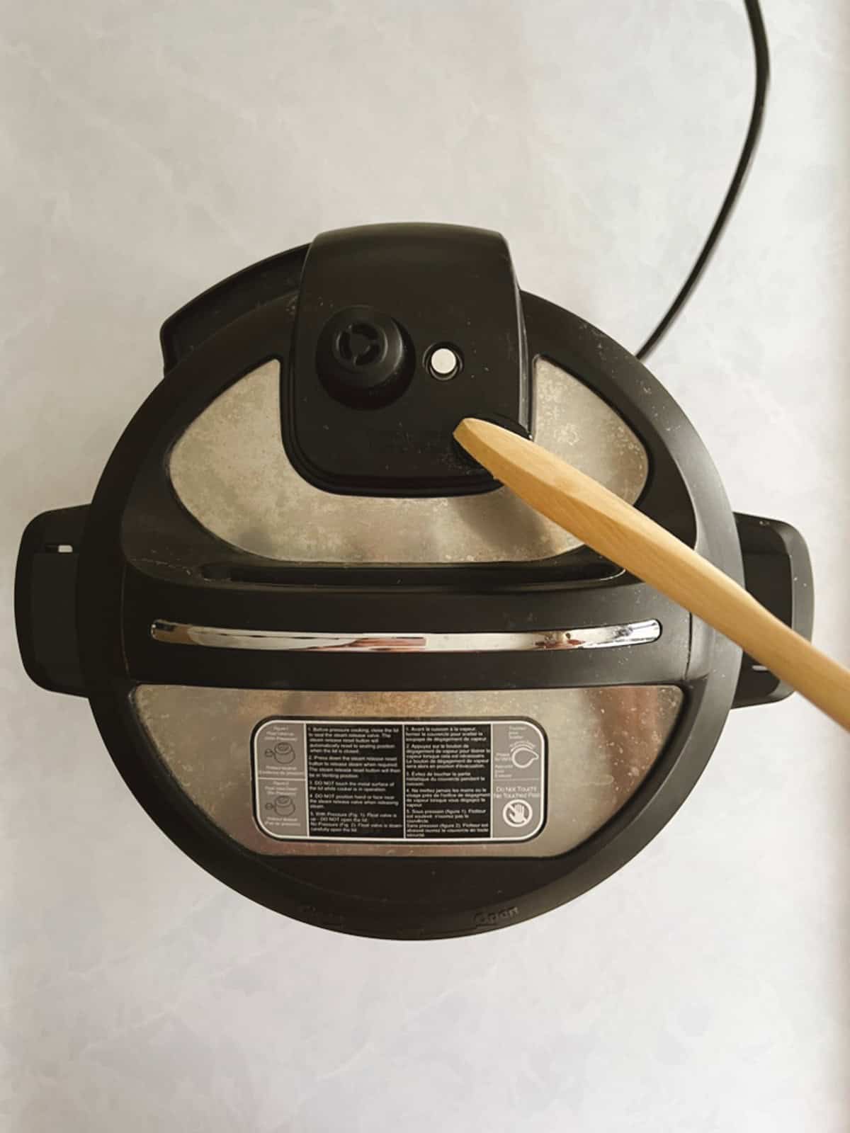 overhead view of closed instant pot with wooden spoon performing quick pressure release