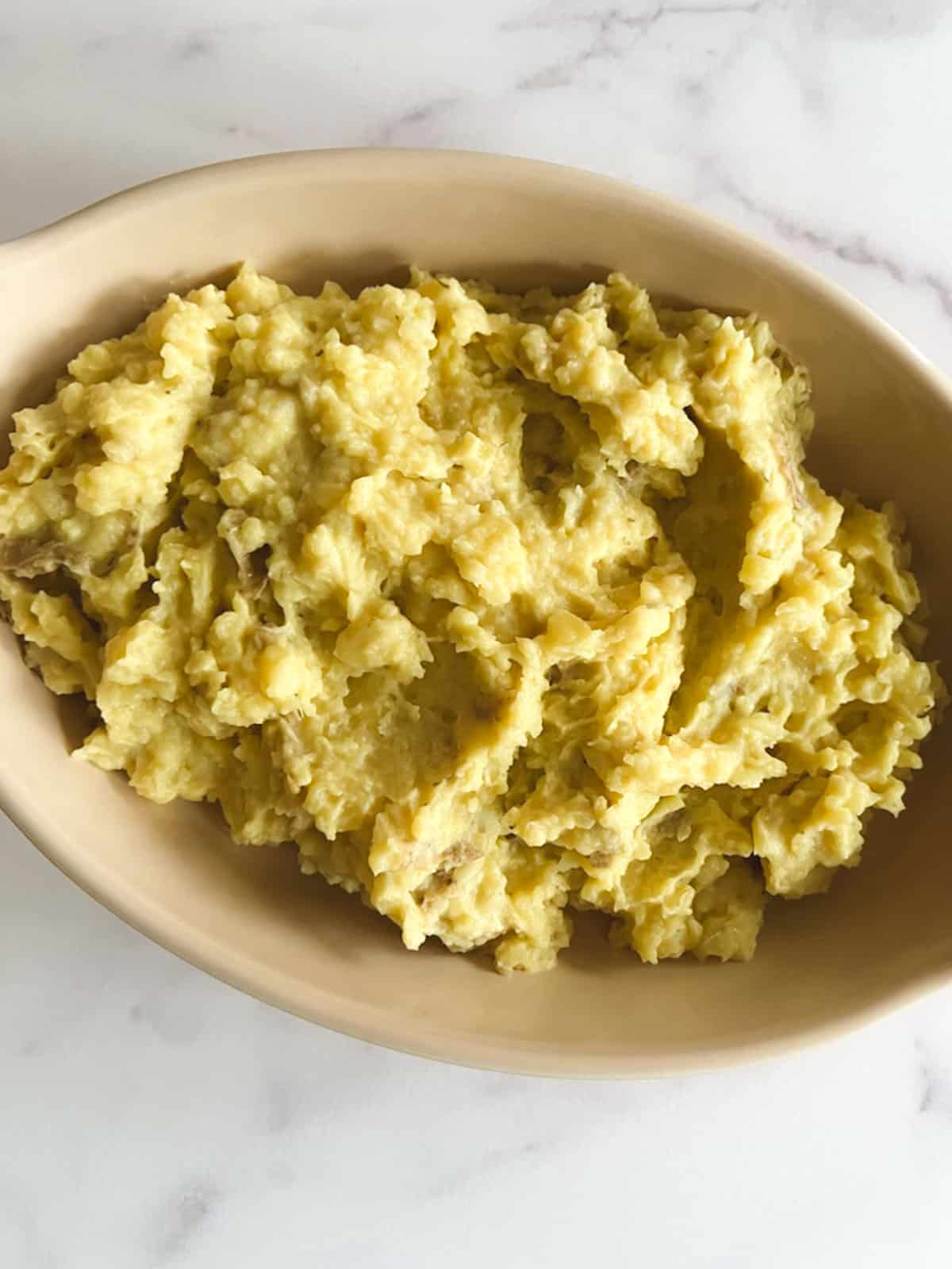 closeup view of oblong serving dish containing vegan instant pot mashed potatoes on a marble background