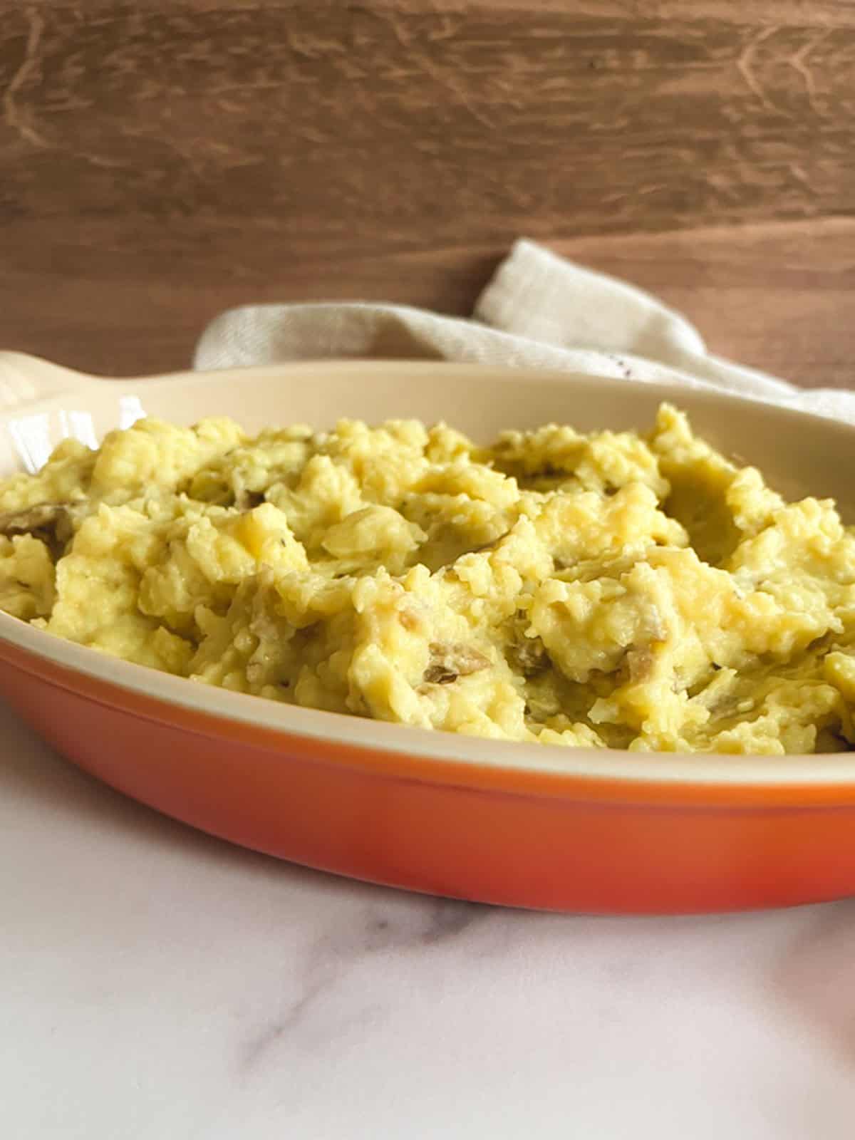 closeup of vegan instant pot mashed potatoes in a shallow orange serving dish against a wooden background