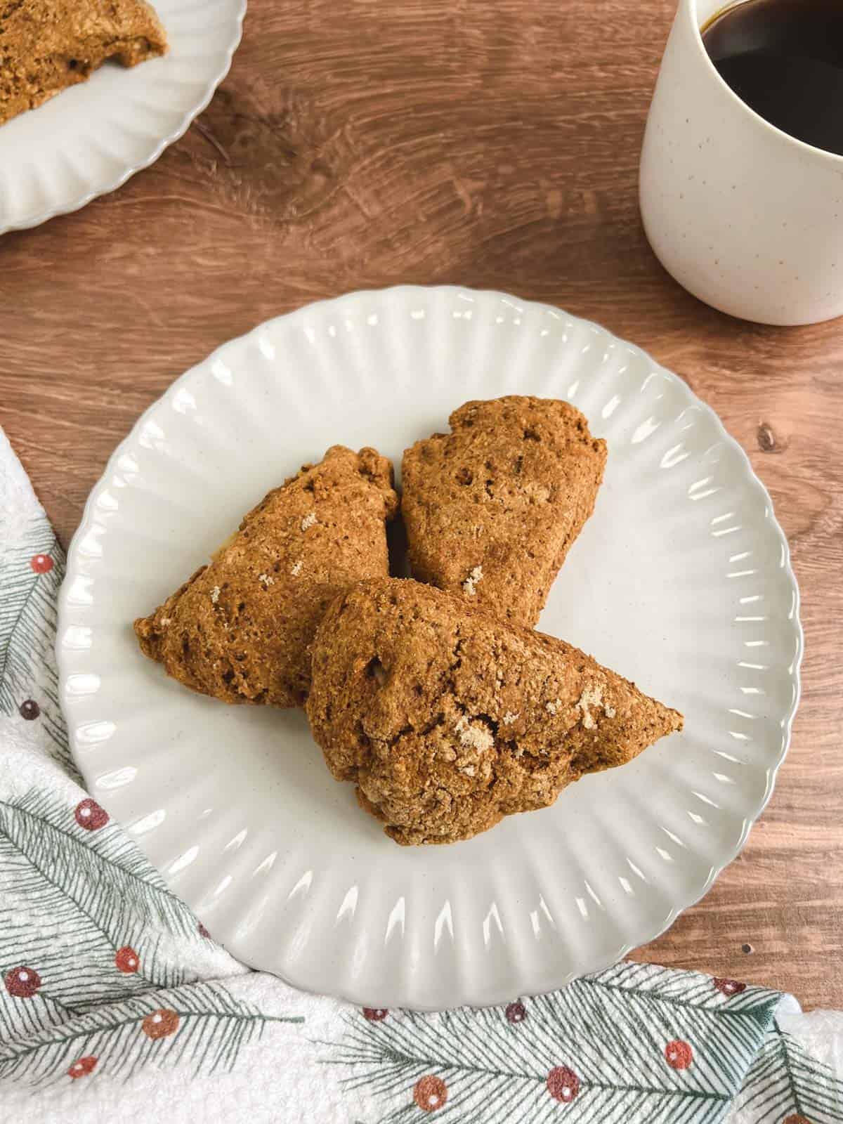 overhead view of three ginger pear scones on an off-white plate with crinkled edges next to a mug of coffee and a festive towel