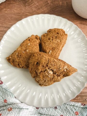 overhead view of a cream-colored plate holding 3 ginger pear scones next to a festive towel