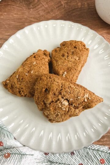 overhead view of a cream-colored plate holding 3 ginger pear scones next to a festive towel