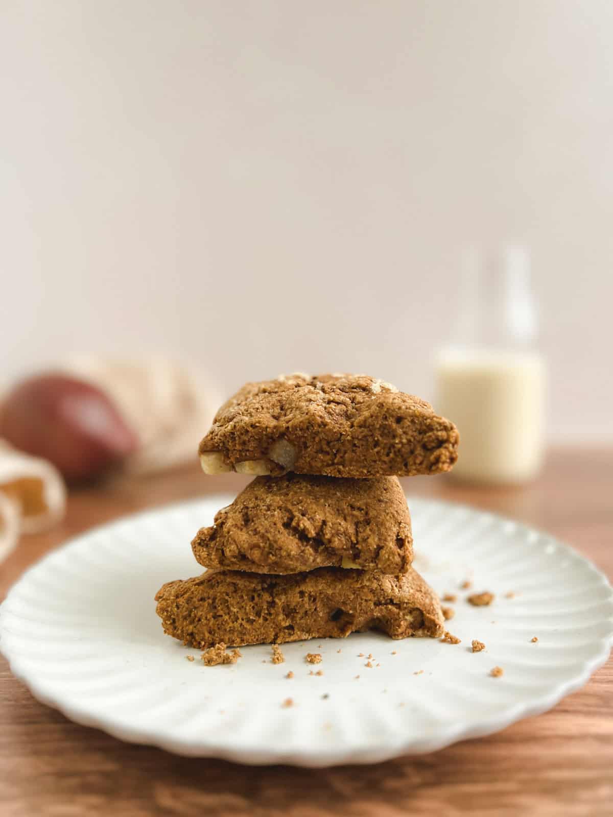 three ginger pear scones stacked on a cream-colored plate with a blurred glass jar of milk and a red pear in the background